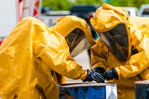 Zwei Personen in Chemikalienschutzanzug verschließen einen Gefahrstoffbehälter