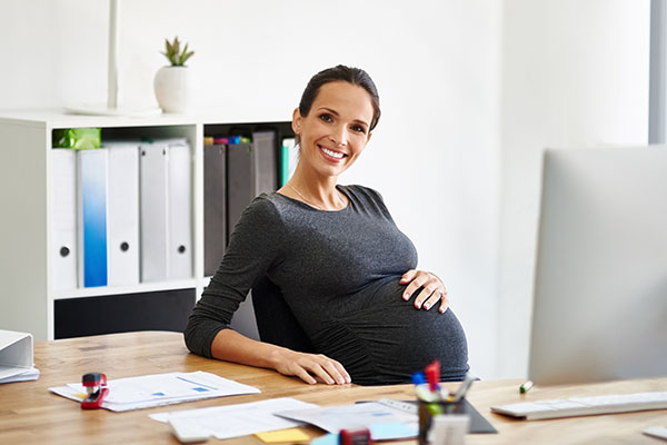 Eine schwangere Frau sitzt am Arbeitsplatz
