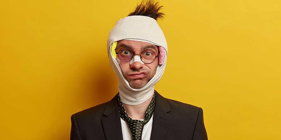 Mann im Anzug mit Verletzungen im Gesicht und Verban am Kopf vor gelbem Hintergrund