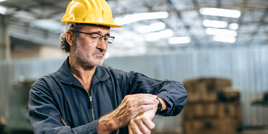 Arbeiter mit Helm im Overall schaut auf die Uhr