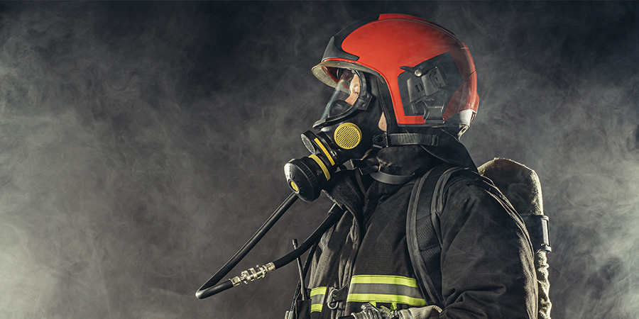 Feuerwehreinsatzkraft in kompletter Schutzausrüstung steht in Brandrauch