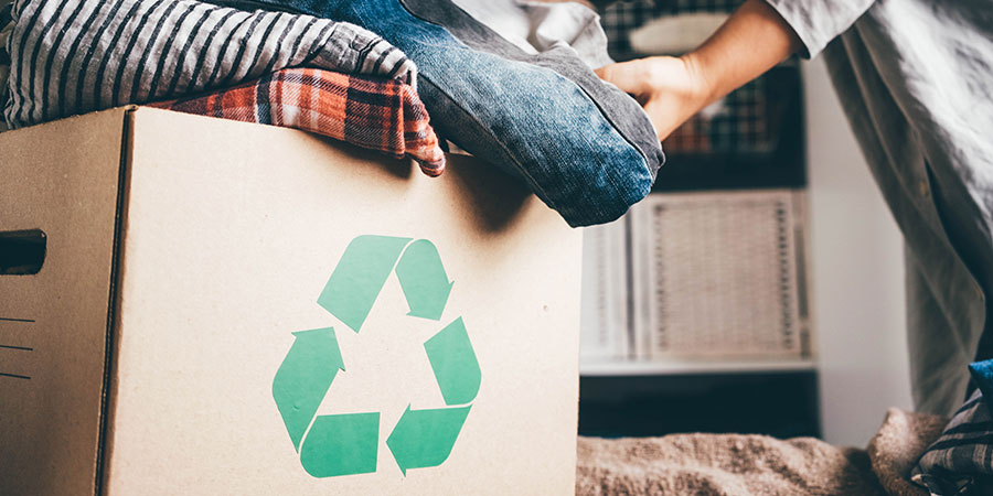 Kleidung wird in Karton mit Recycling-Symbol gepackt